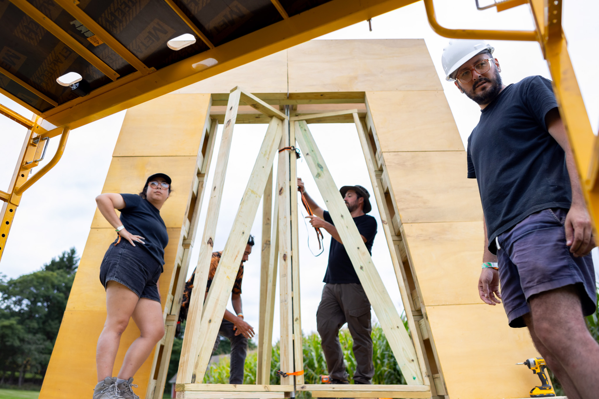 The four faculty leads fitting the vane into the wooden doorway, seen from below a scaffold