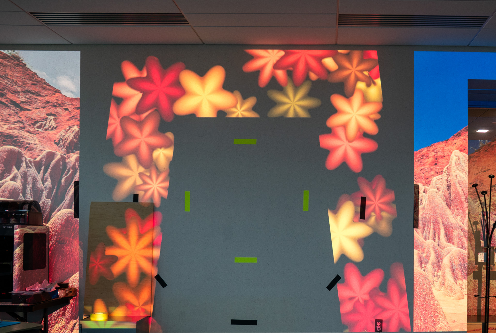 The flower field projected on an office wall inside the frame's outline, with calibration tape marks and a plywood test panel leaning at the lower left